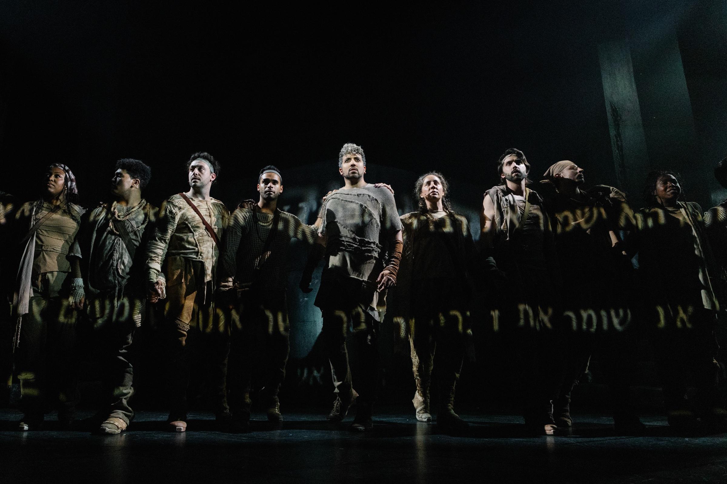 The company of Jesus Christ Superstar advancing downstage in a line, in near darkness