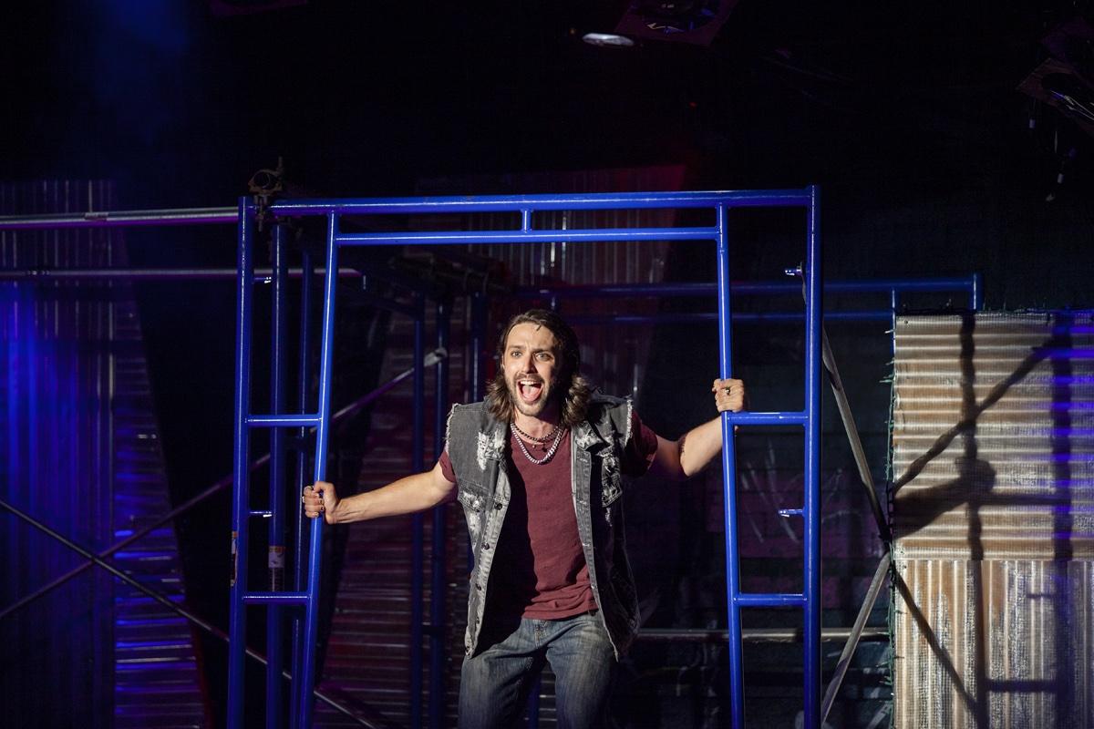 Shane Lonergan as Roger on the scaffolding set of Rent, arms flung wide