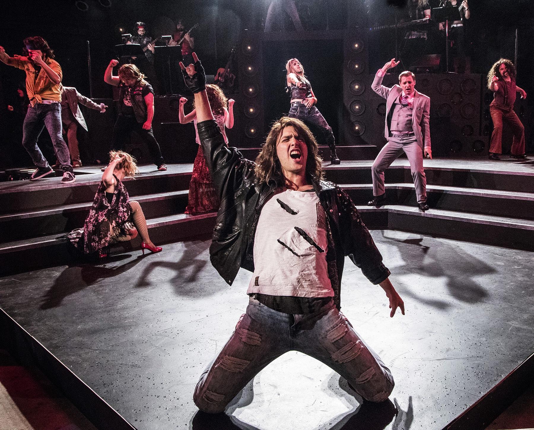 Shane Lonergan as Drew on his knees centre stage, mid-number, the company arranged on the steps behind him