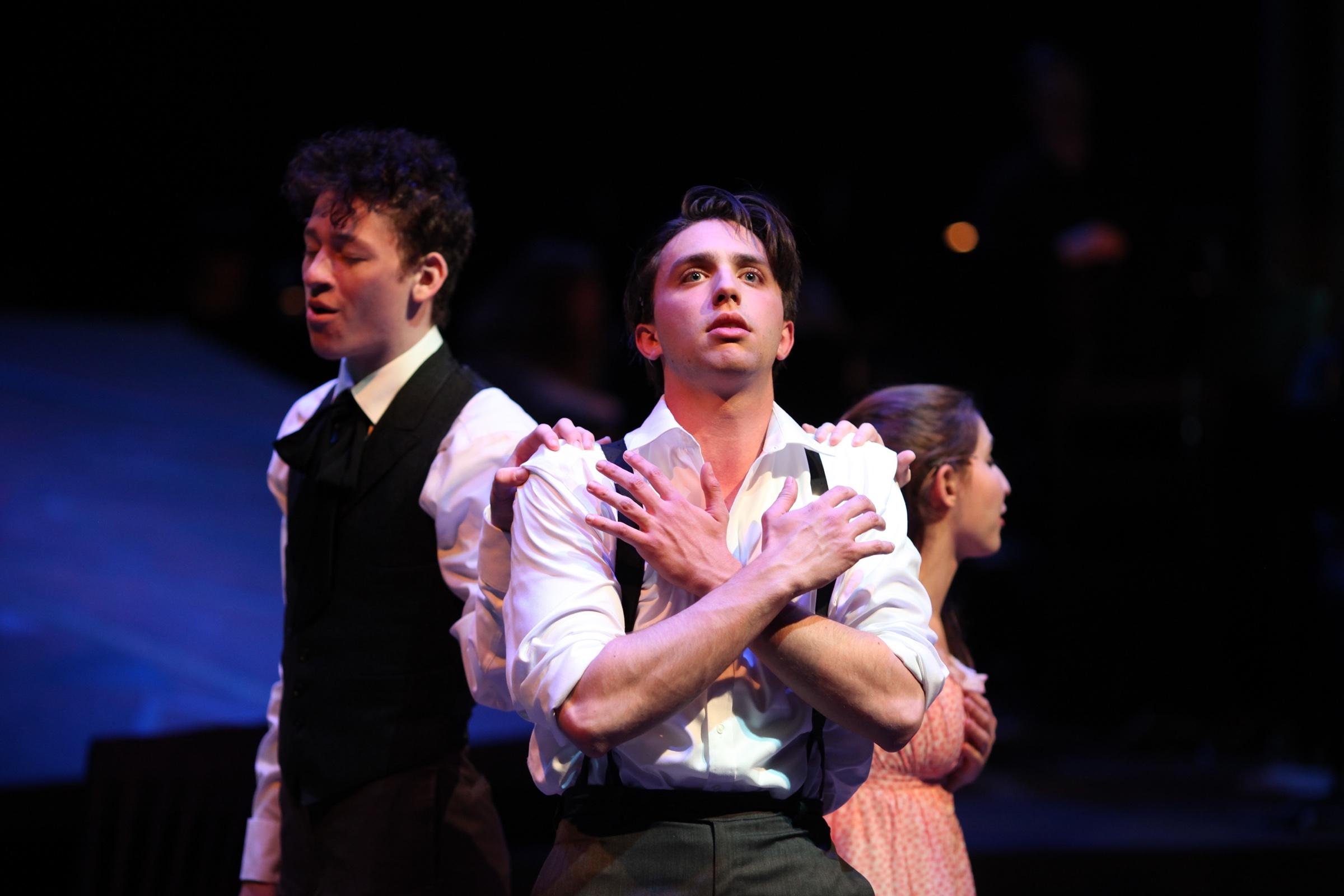 Shane Lonergan as Melchior with his arms crossed over his chest, flanked by the company in blue light